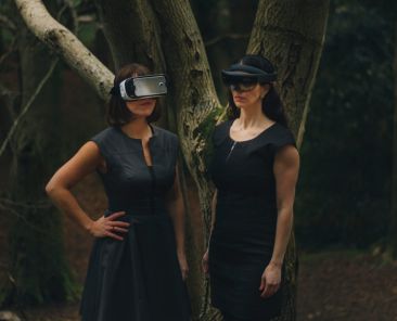 Two women wearing VR headsets in a wooded setting
